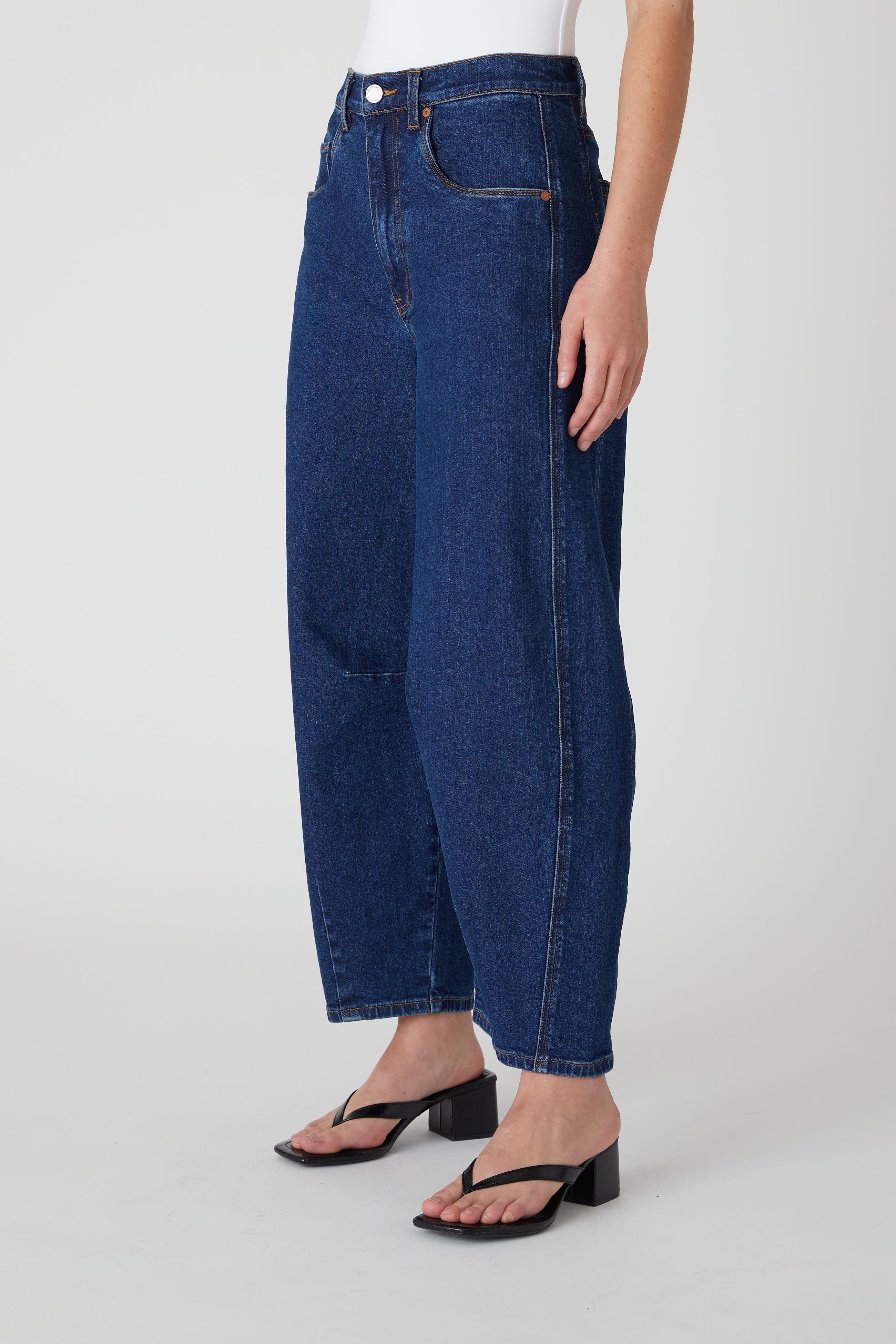 Side view of a model wearing the BLANKNYC Deep Down Barrel Jean in Dark Indigo.