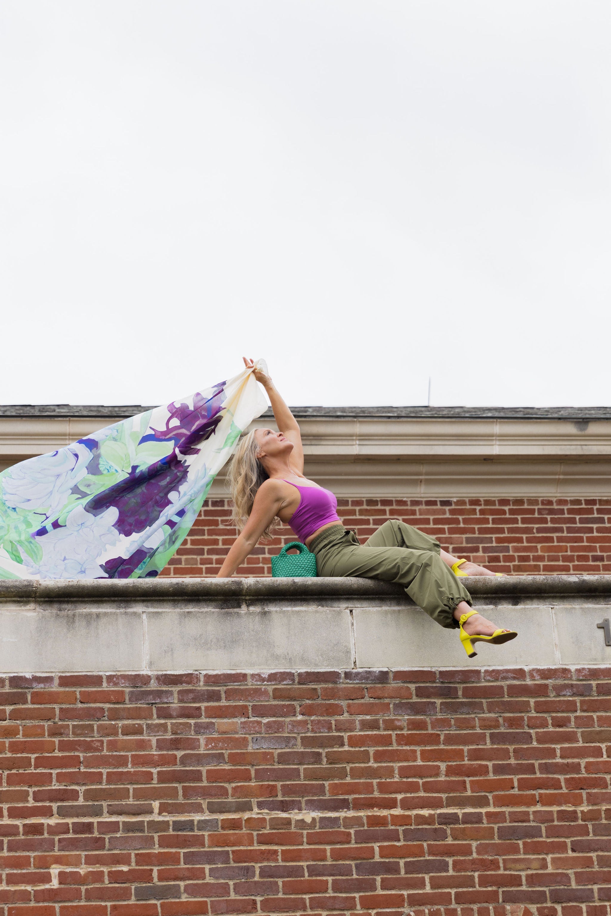 Side view of a model wearing the Be Fit Convertible Cargo Pant in green, showing the cargo pockets and adjustable bungee hems, atop a brick building.