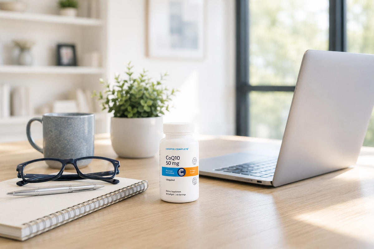 A bottle of Cooper Complete CoQ10 50 mg on a home office desk with a laptop, notebook, glasses, and coffee mug, supporting heart health and cellular energy production.