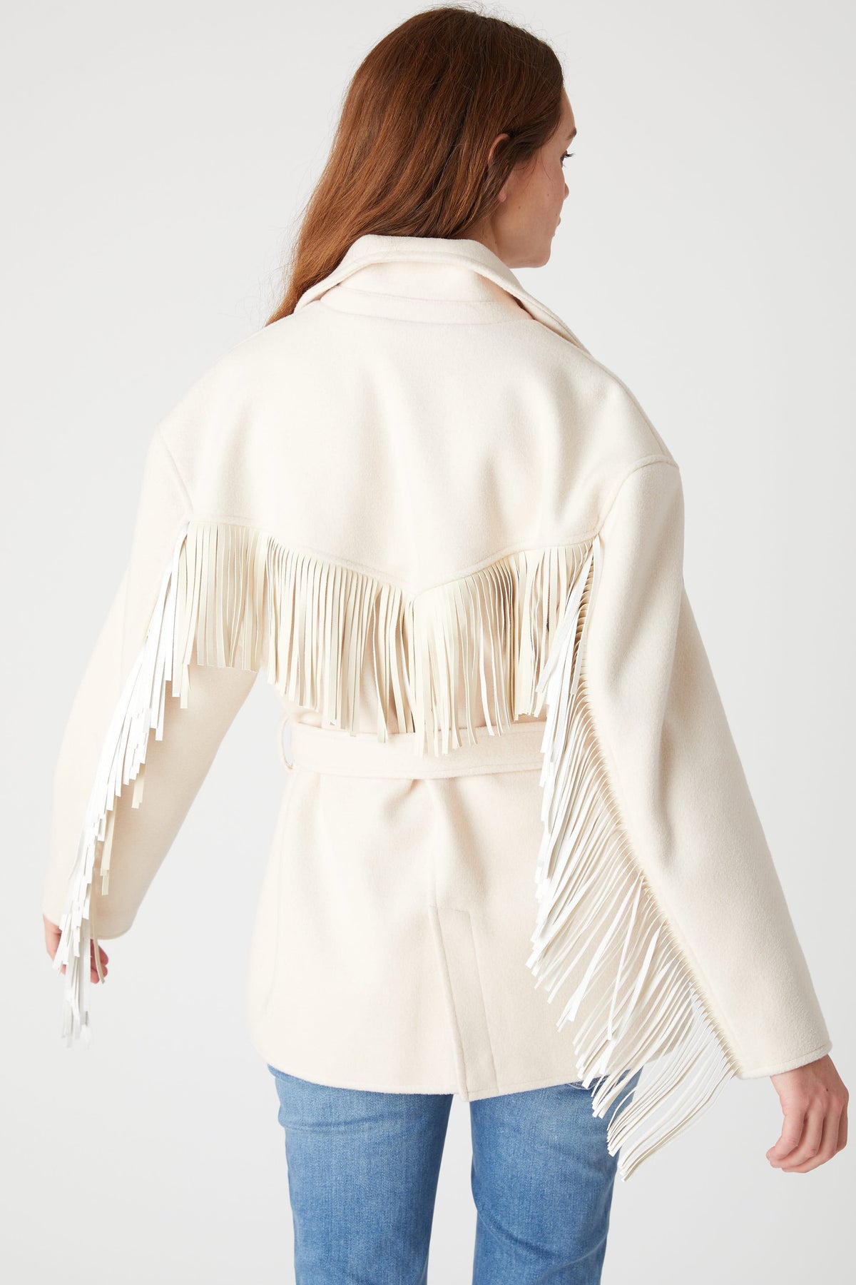 Back view of a model wearing the BLANK NYC Rodeo Star Blazer in Off White, showing fringe across the back and sleeves.