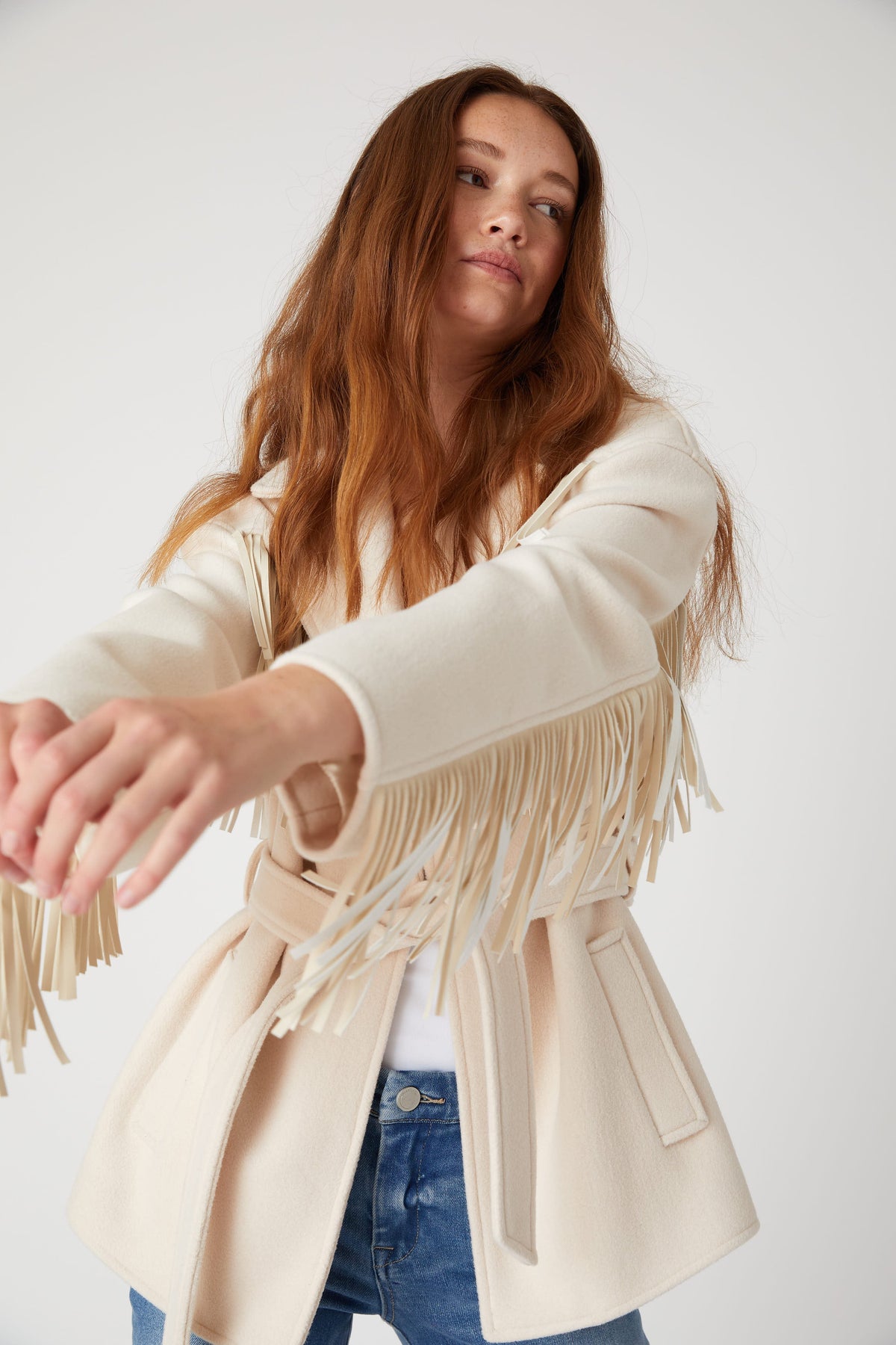 Detail view of the BLANK NYC Rodeo Star Blazer in Off White, showing sleeve fringe, the waist belt and a side pocket.