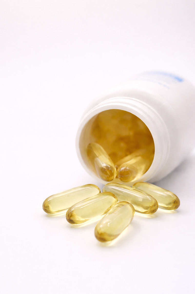 Softgels spilling out of a bottle of Cooper Complete Advanced Omega-3 supplements onto a white background.