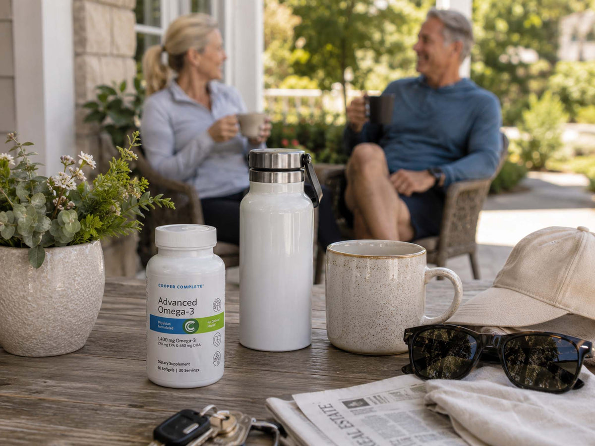 Cooper Complete Advanced Omega-3 softgels on a patio table with a water bottle and coffee mug as a couple relaxes outdoors.