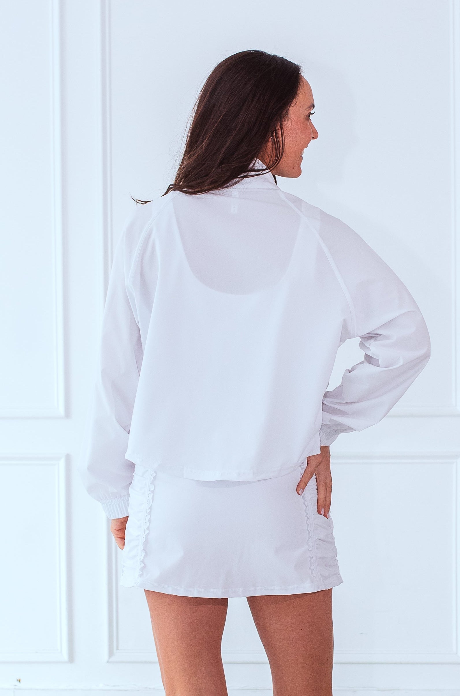 Back view of smiling, active, middle-aged woman in white activewear wearing the Brooklyn Jacket in White.