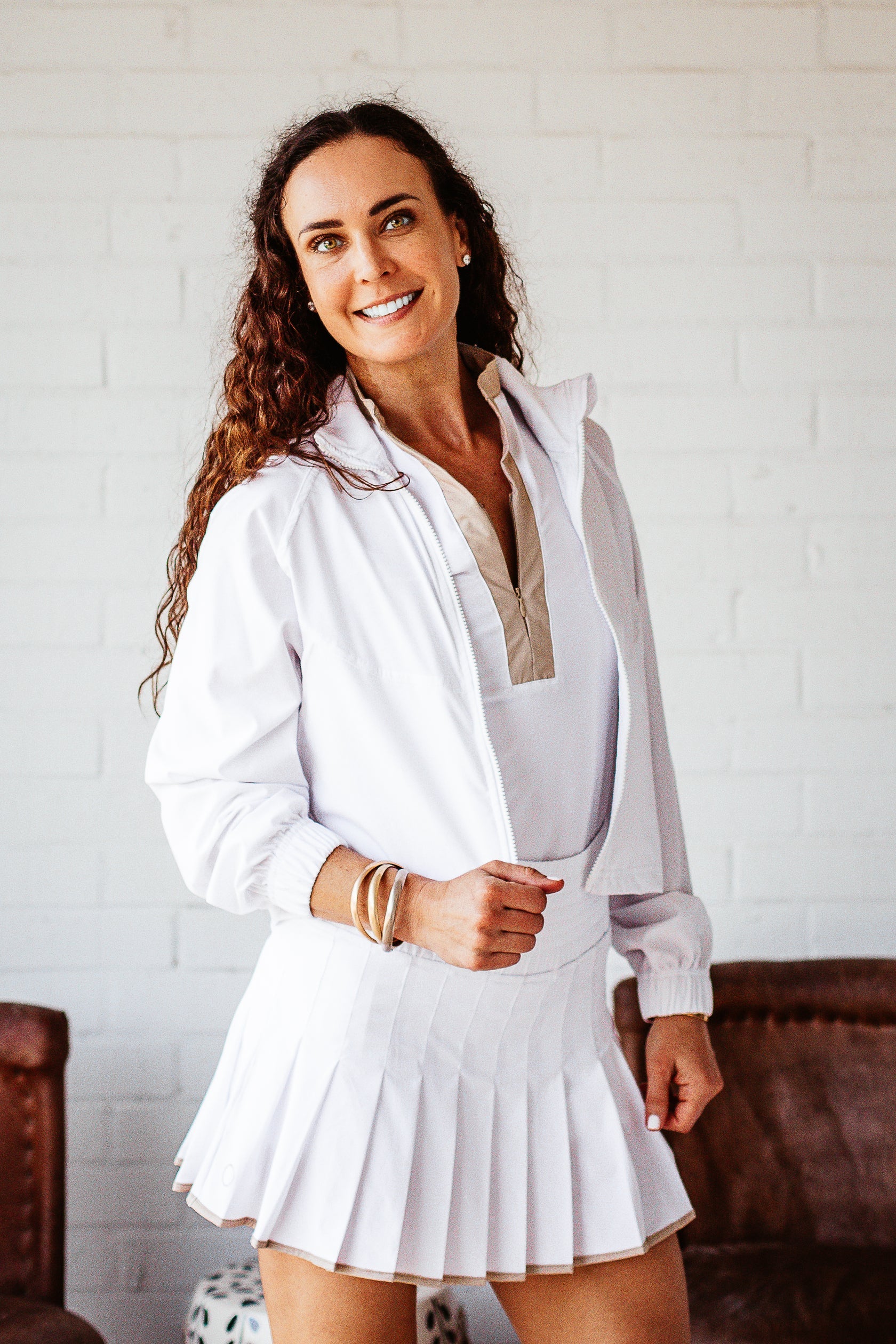 Front view of smiling, active, middle-aged woman in white activewear wearing the Brooklyn Jacket in white.