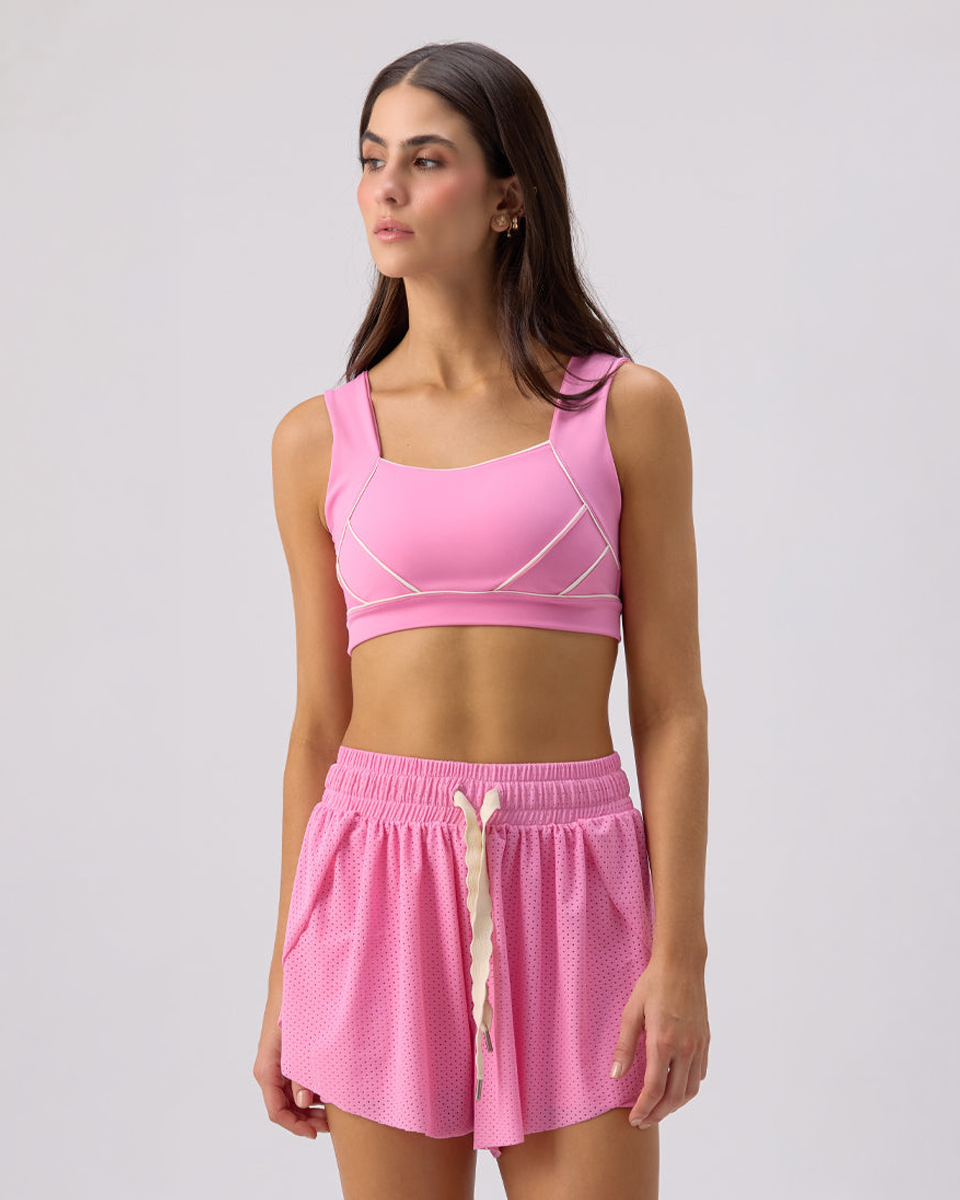 Woman wearing a Glee x Be Fit pink sports bra and shorts set on a light gray background