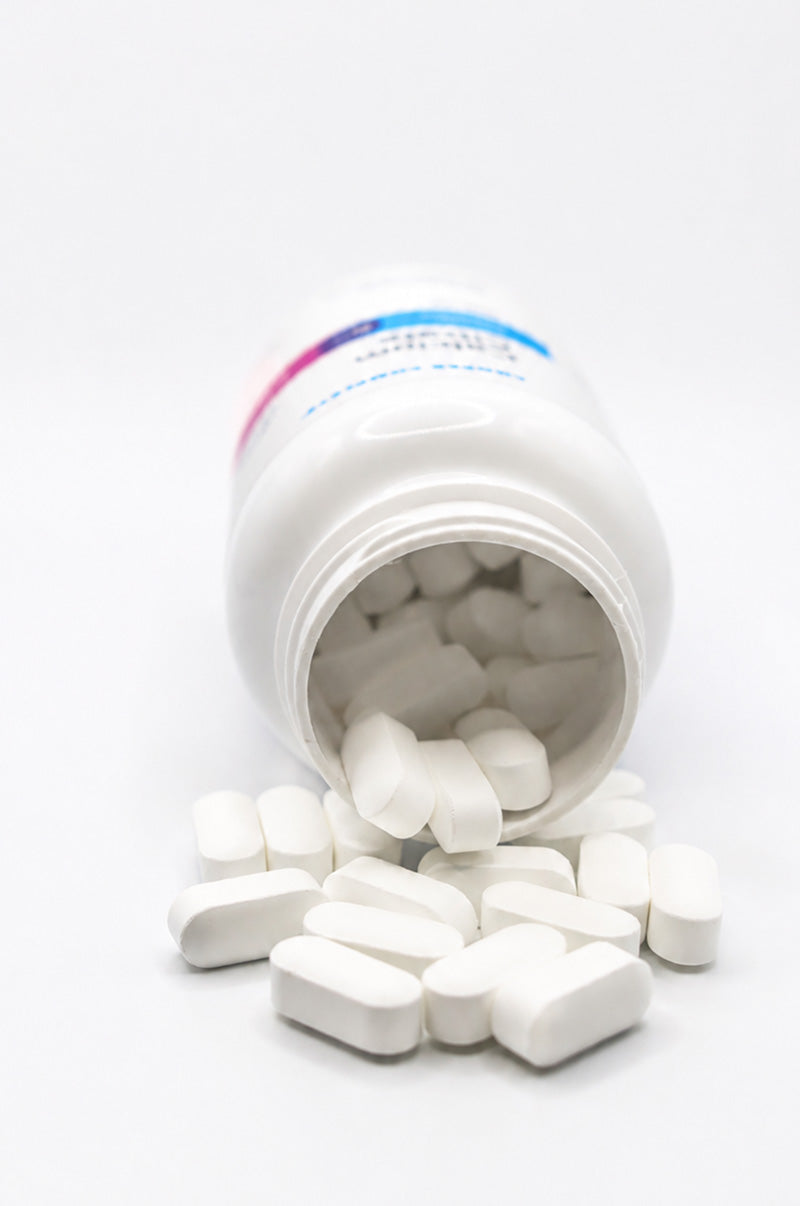 Open white Cooper Complete Calcium Citrate pill bottle with tablets spilling out on a white background.