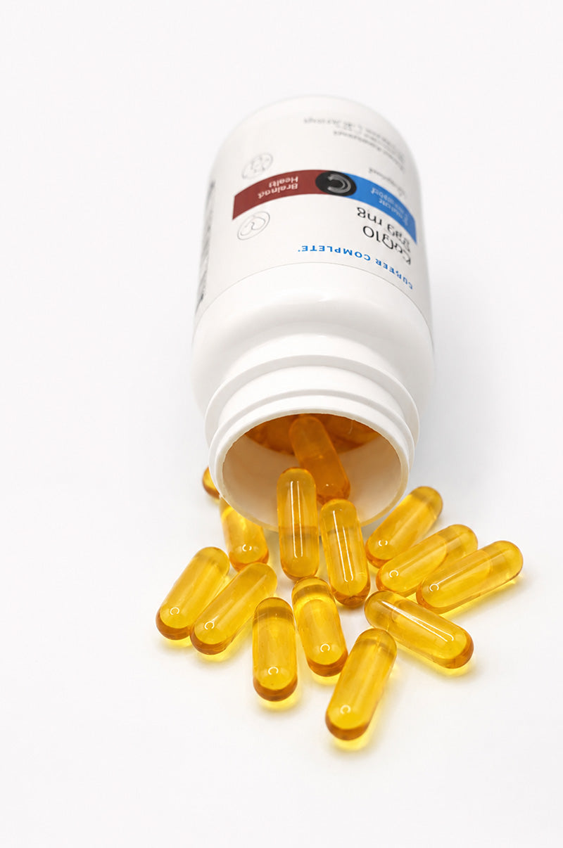 Open white Cooper Complete 100 mg CoQ10 Ubiquinol pill bottle with capsules spilling out on a white background