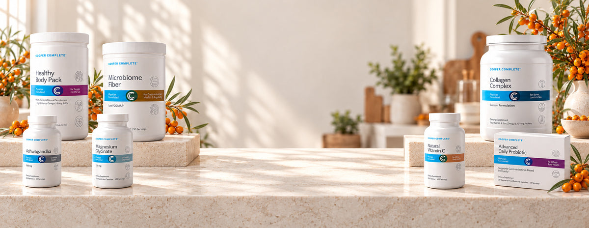 Cooper Complete Healthy Body Pack, Microbiome Fiber, Collagen Complex, Ashwagandha, Magnesium Glycinate, Natural Vitamin C, and Advanced Daily Probiotic displayed on a sunlit stone kitchen counter with seaberry decor.