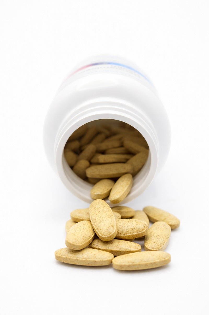 Open white Cooper Complete Dermatologic Health pill bottle with tablets spilling out on a white background