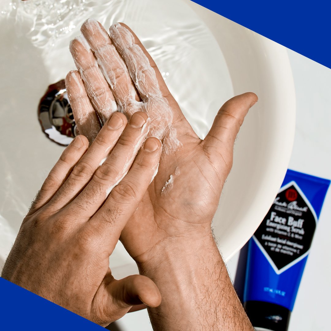 Jack Black Face Buff Scrub being worked between wet hands beside a sink, showing the creamy exfoliating formula during use.