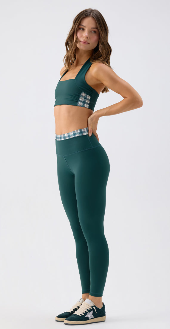 Side view of a model wearing the Be Fit x Glee botanic green Verdant Leggings with a high-rise plaid waistband.