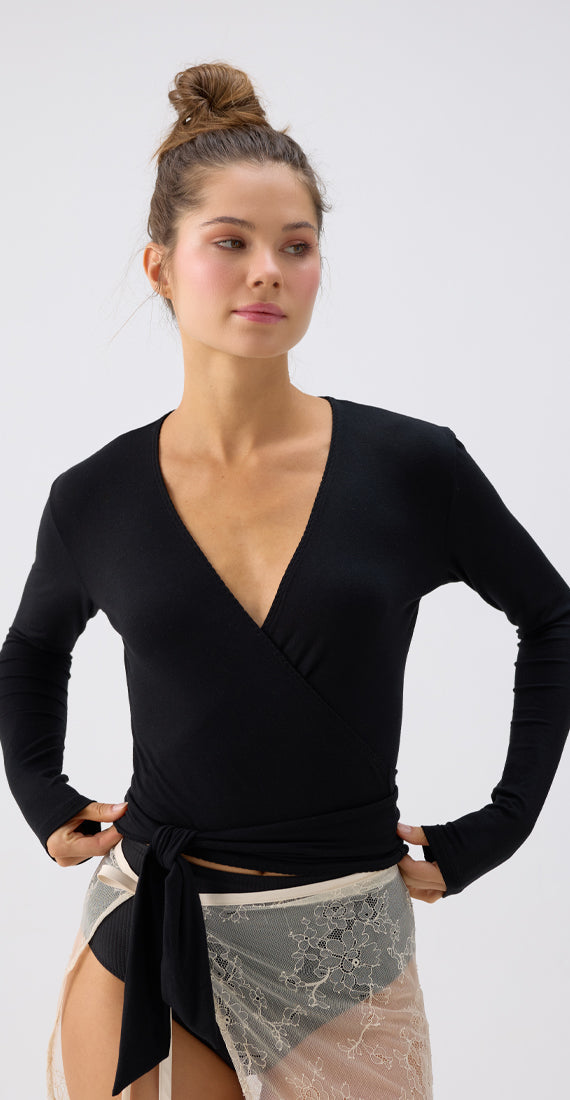 Front view of a model wearing the black onyx Be Fit x Glee Ballerina Wrap with long sleeves and a tied waist.
