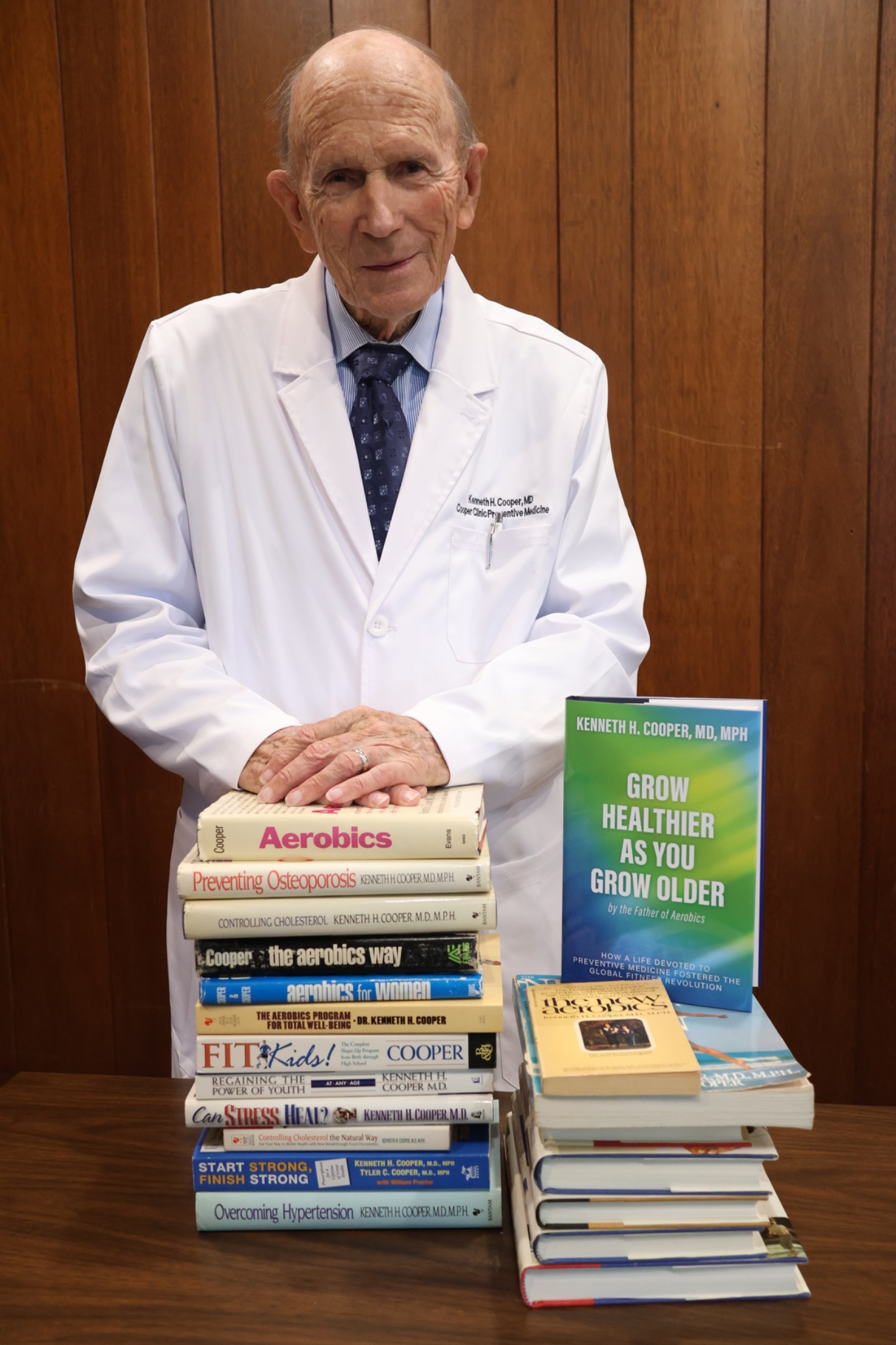 Kenneth H. Cooper, MD, MPH, in a white physician coat with his latest book Grow Healthier as You Grow Older