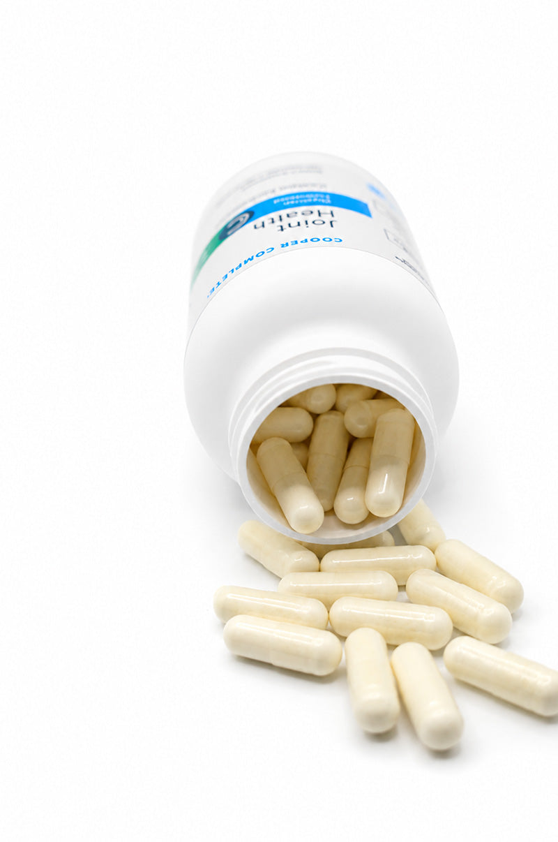 Open white Cooper Complete Joint Health Supplement pill bottle with capsules spilling out on a white background