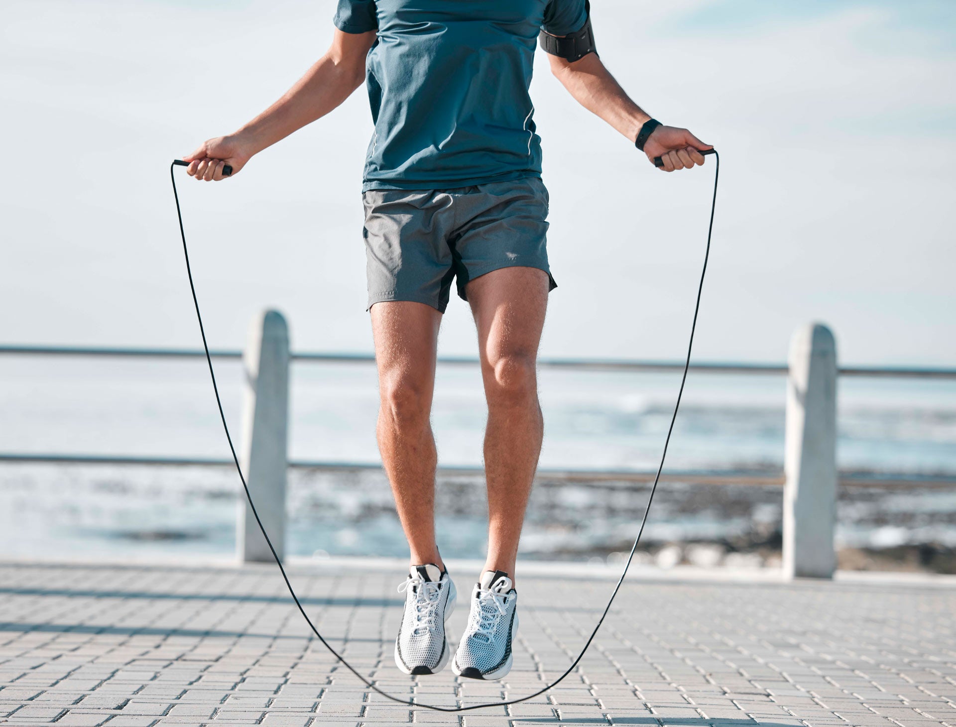 Person exercising with a jump rope outdoors on a waterfront path as part of an active lifestyle.