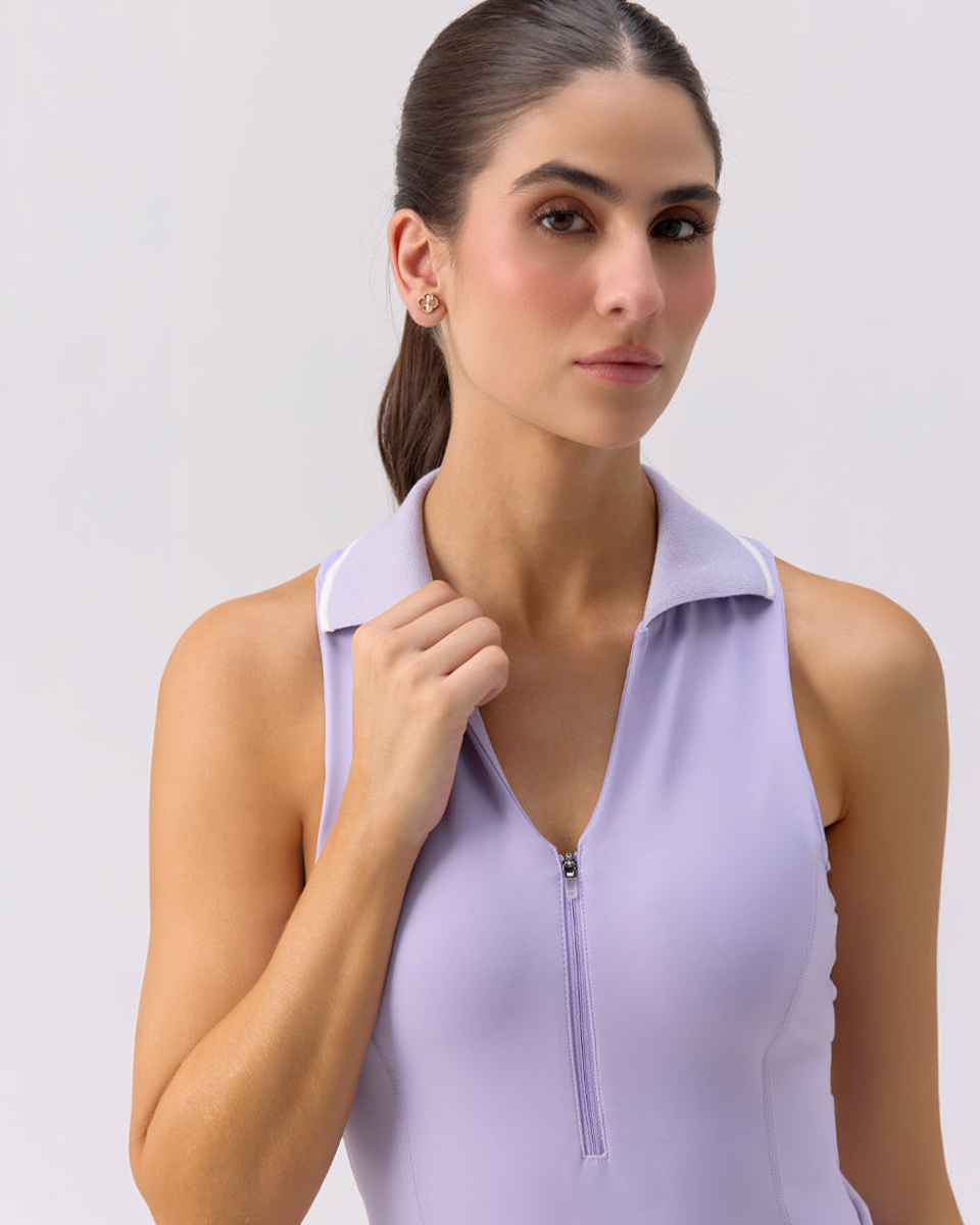 Close-up of a woman wearing a Glee Be Fit light purple sleeveless tennis or pickleball dress with a zipper on a plain background