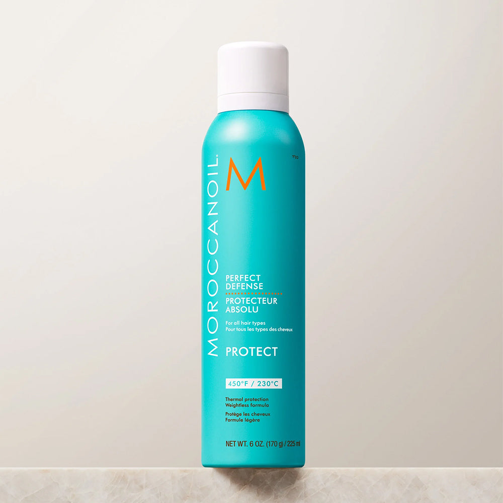 A turquoise Moroccanoil Protect hairspray aerosol can with a white cap, standing upright on a light marble surface against a neutral off-white background.