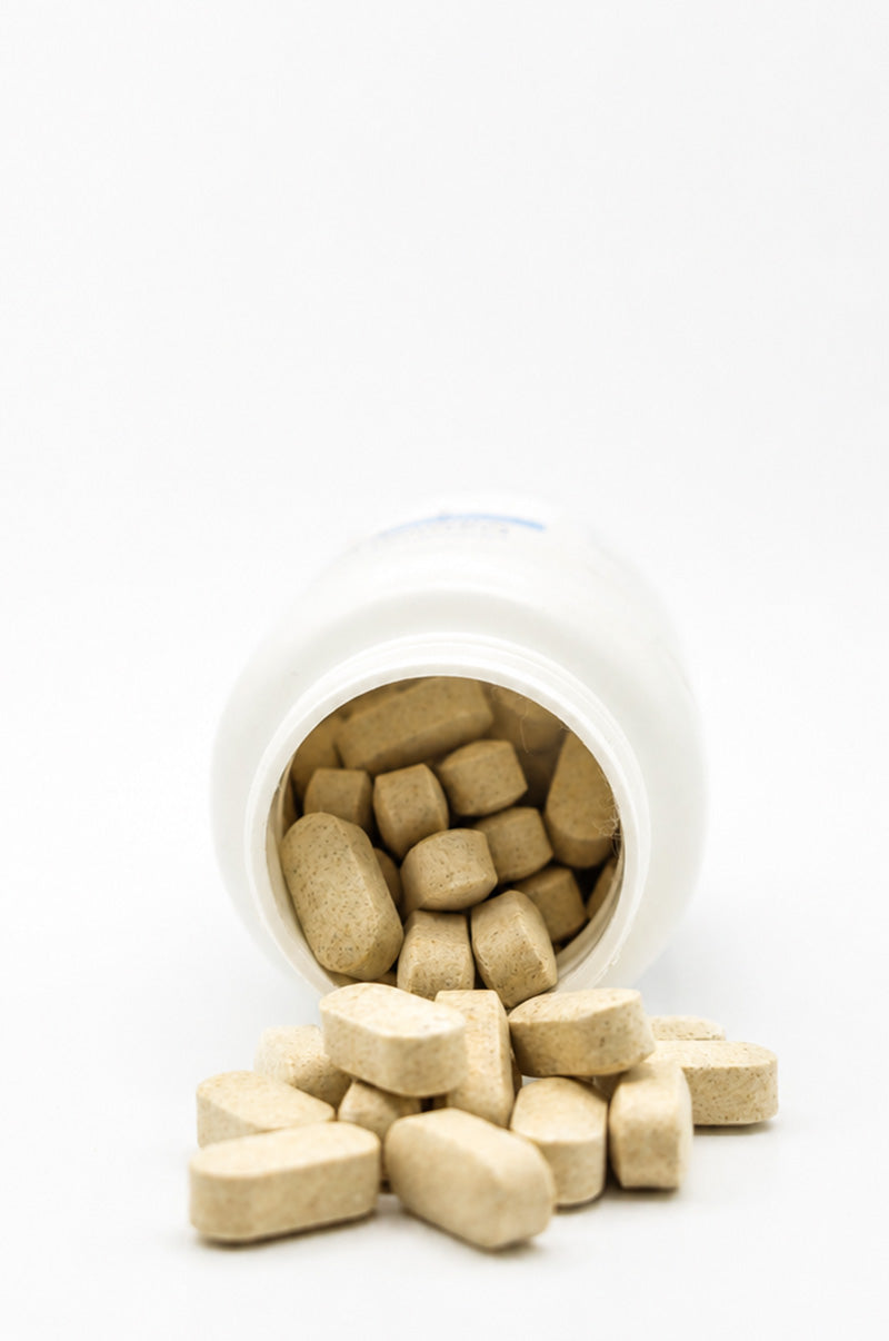 Open white Cooper Complete Natural Vitamin C Supplement pill bottle with tablets spilling out on a white background