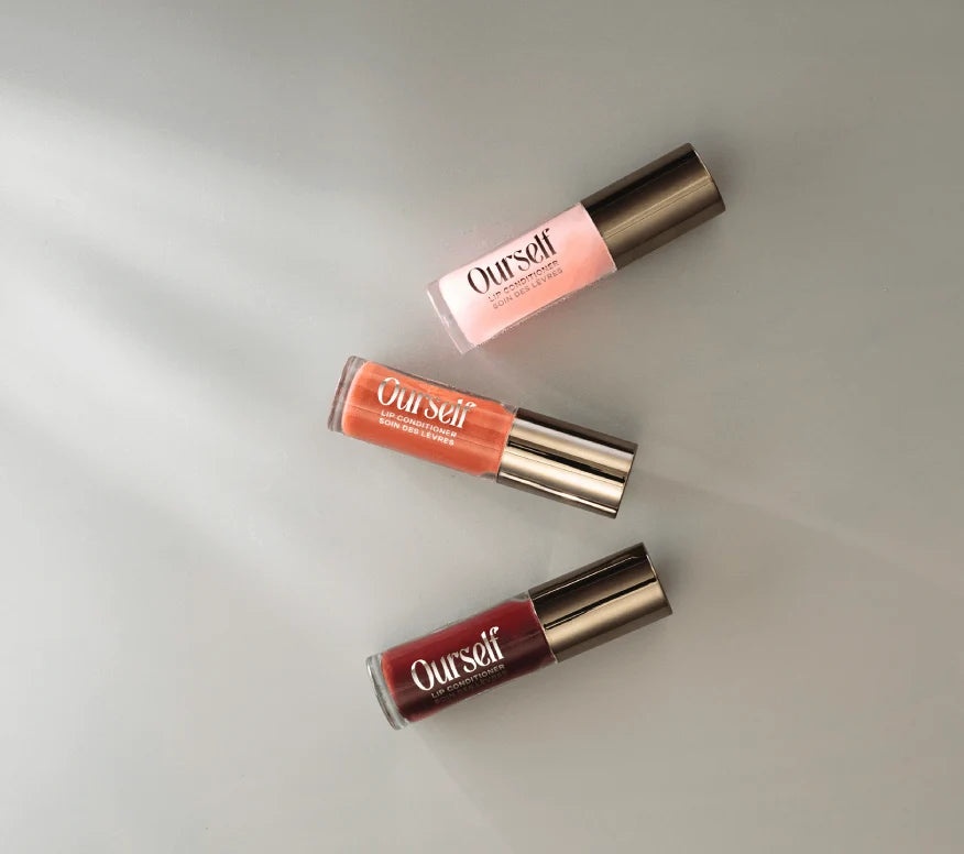 Ourself Lip Conditioner Trio in shades Clear, Sunset, and Berry on a light grey, sunlit background.