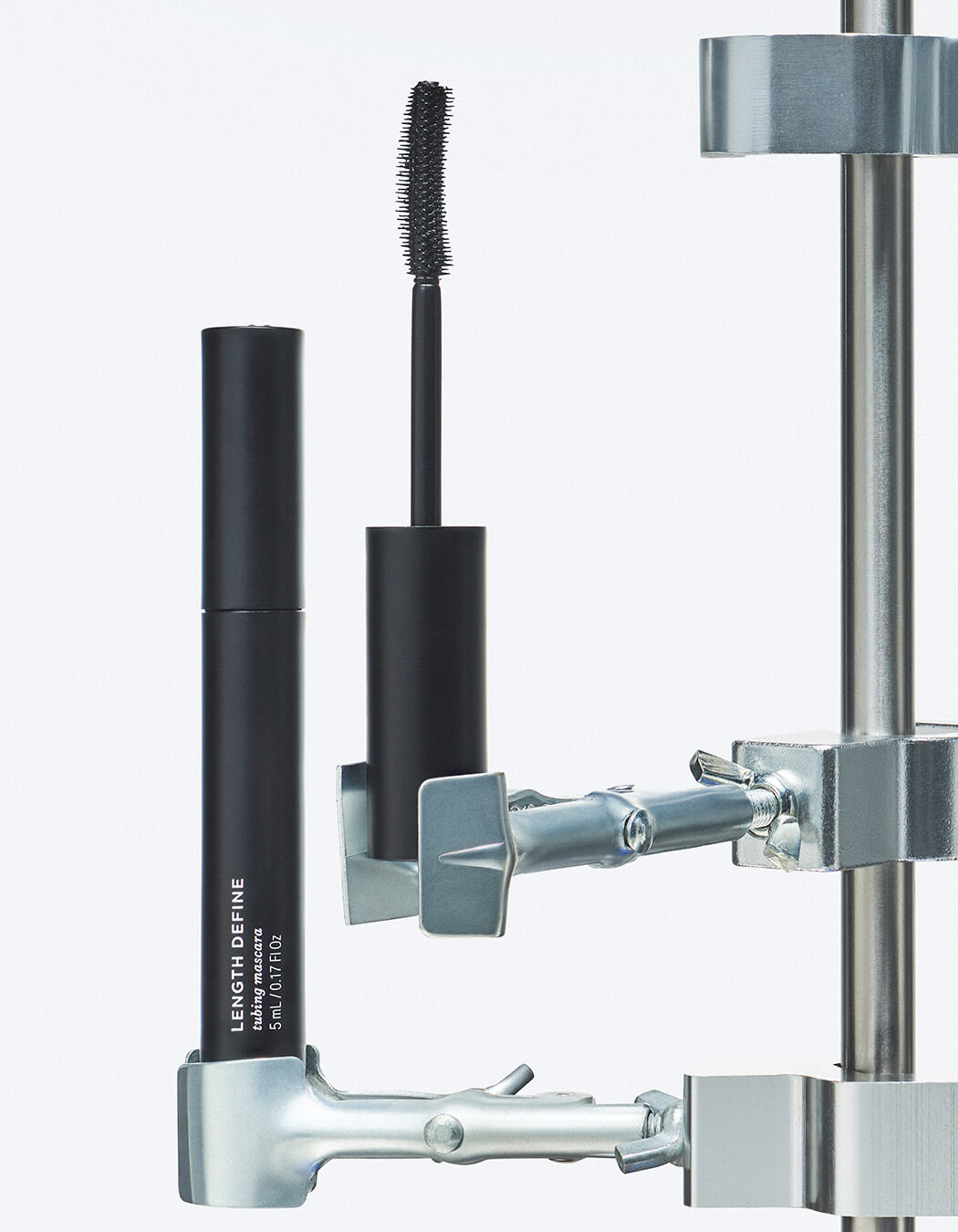 Silver tools holding black bottle of RevitaLash Length Define Tubing Mascara.
