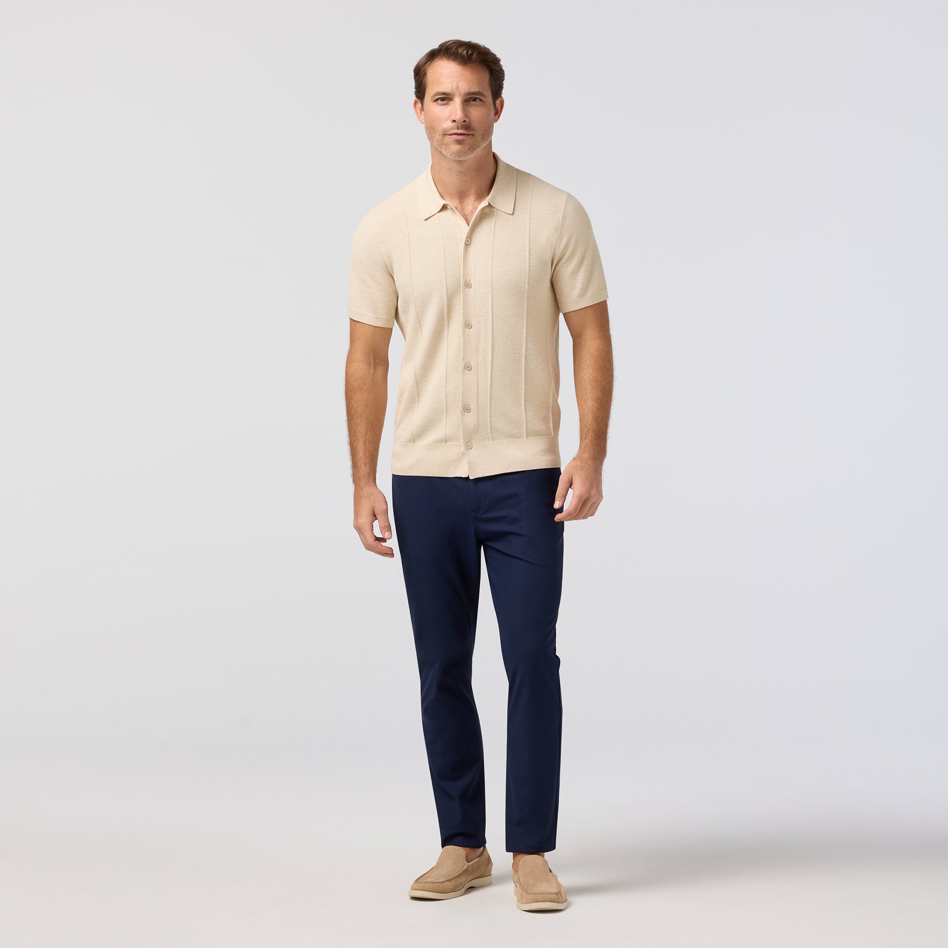 Man wearing Mizzen+Main Ashe Short Sleeve Polo Sweater (Trim Fit) in beige, a men's short-sleeve textured knit polo sweater with button-front styling and breathable COOLMAX® fabric.
