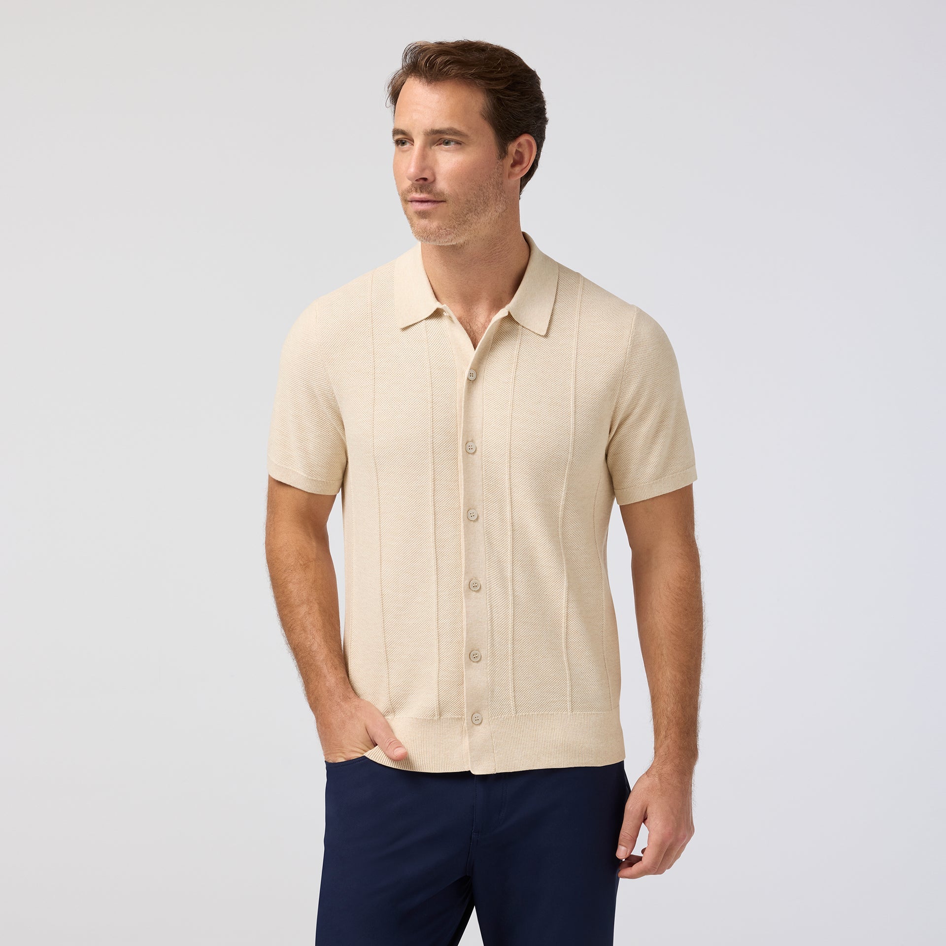 Man wearing Mizzen+Main Ashe Short Sleeve Polo Sweater (Trim Fit) in beige, a men's short-sleeve textured knit polo sweater with button-front styling and breathable COOLMAX® fabric.