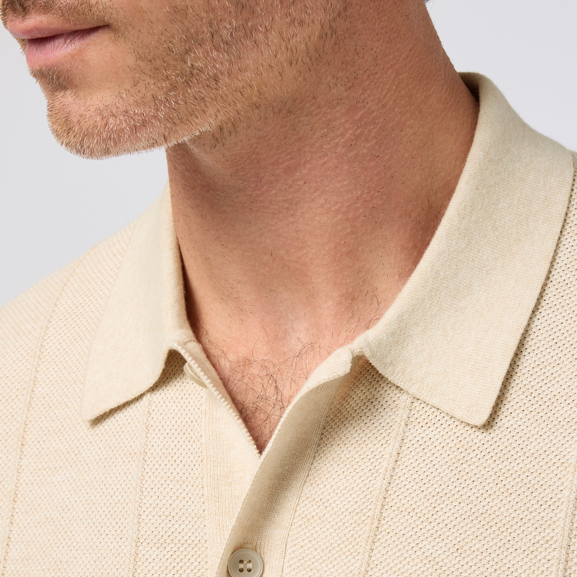 Close-up of the neckline of the Mizzen+Main Ashe Short Sleeve Polo Sweater (Trim Fit) in beige, a men's short-sleeve textured knit polo sweater with button-front styling and breathable COOLMAX® fabric.