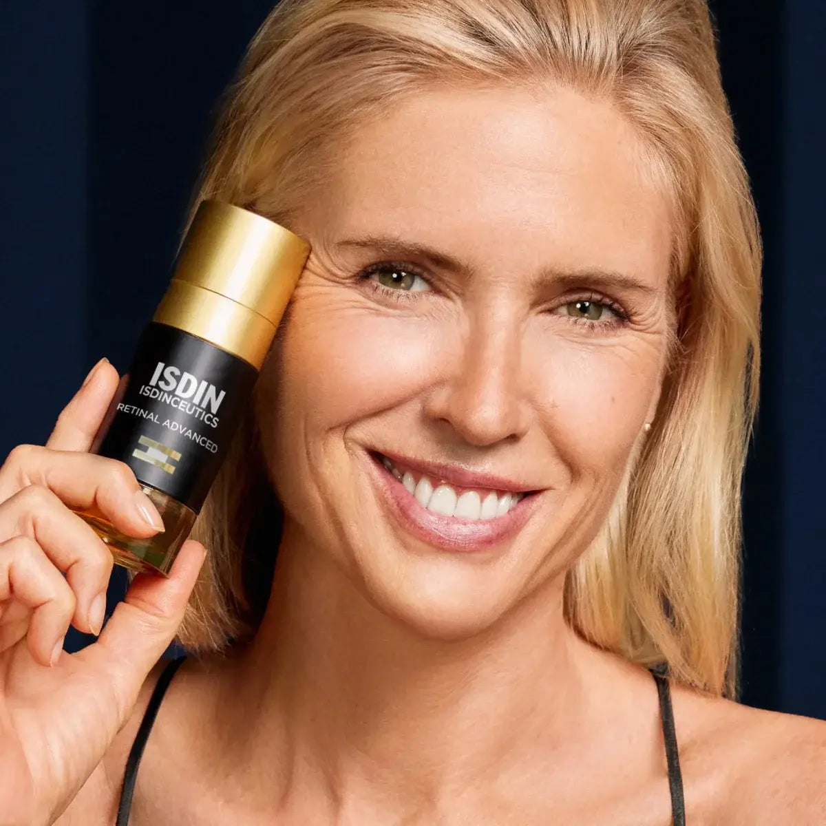 Middle aged woman with healthy-looking skin holding a bottle of ISDINCEUTICS Retinal Advanced close to her face.