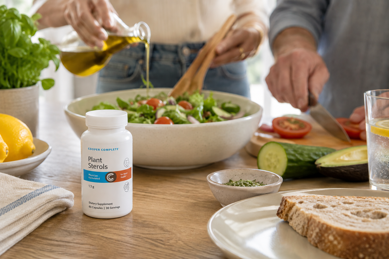 A bottle of Cooper Complete Plant Sterols supplement bottle on a kitchen counter beside a fresh salad as two adults prepare a healthy meal.