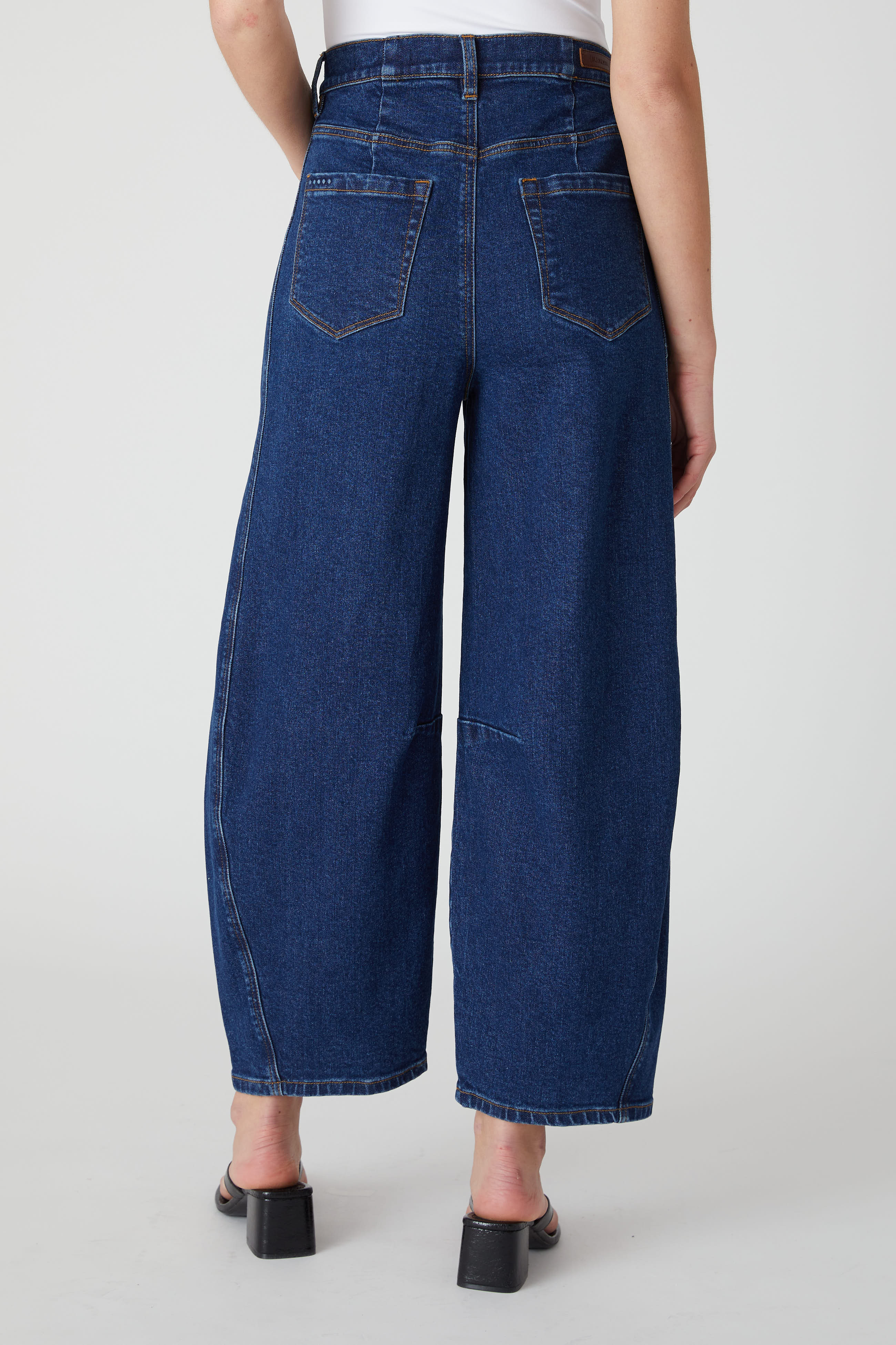 Back view of a model wearing the BLANKNYC Deep Down Barrel Jean in Dark Indigo.