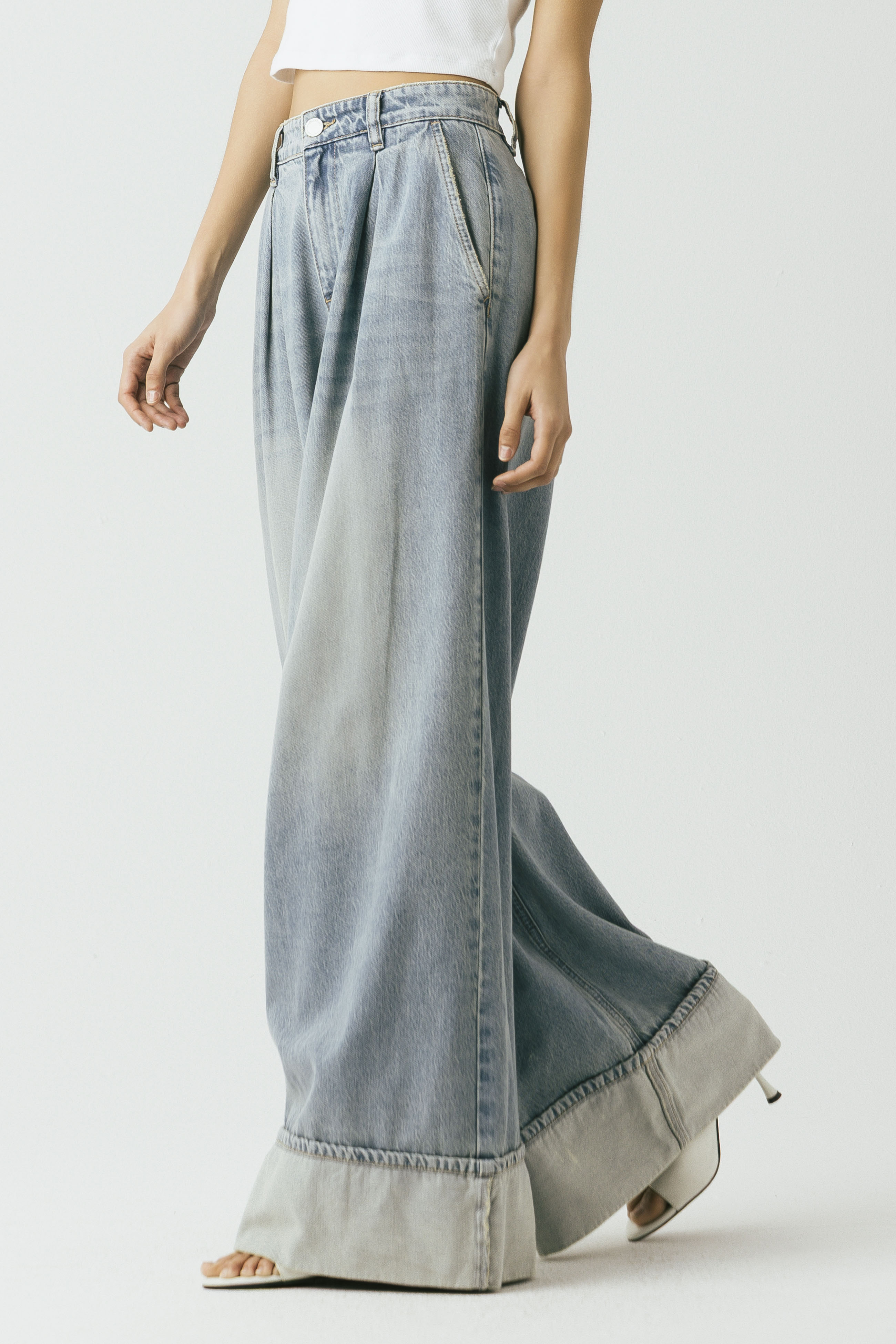 Side view of a model wearing the Blank NYC Easy Day Pleated Wide-Leg Denim Trouser in Light Indigo Creative.