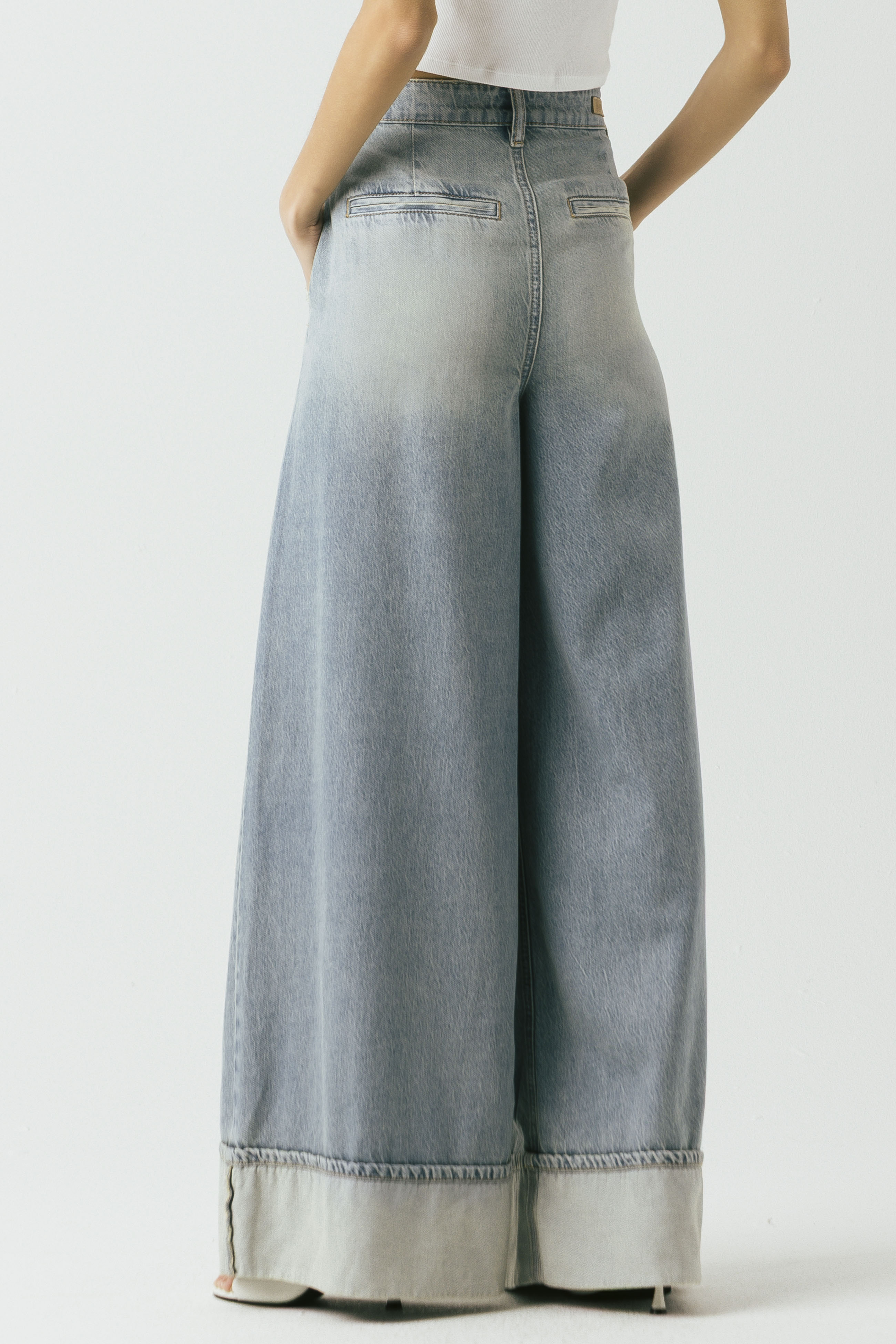 Back view of a model wearing the Blank NYC Easy Day Pleated Wide-Leg Denim Trouser in Light Indigo Creative.