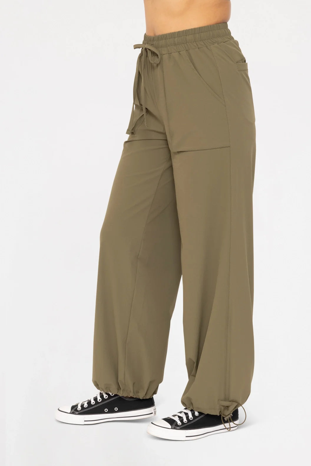 Side view of a model wearing the Be Fit Convertible Cargo Pant in green, showing the cargo pockets and adjustable bungee hems.