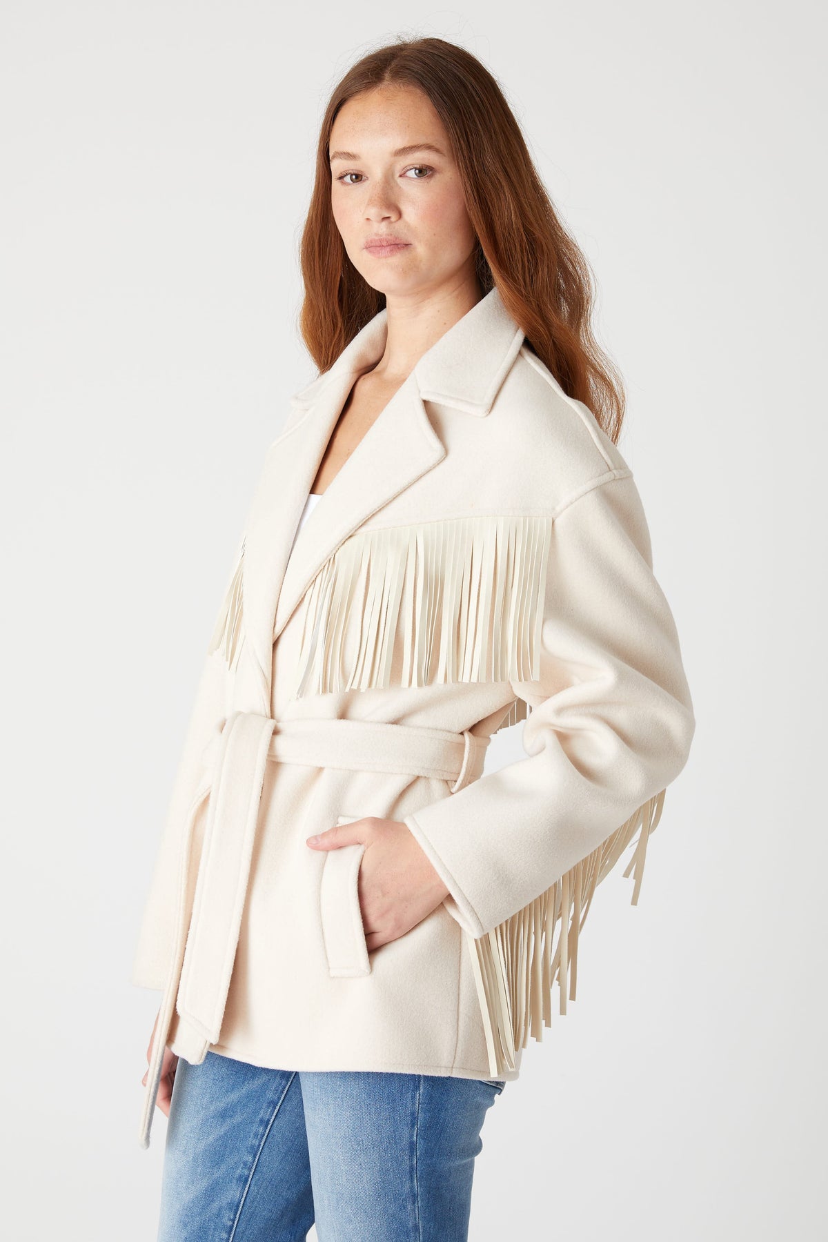 Angled front view of a model wearing the BLANK NYC Rodeo Star Blazer in Off White, showing fringe and a side pocket.