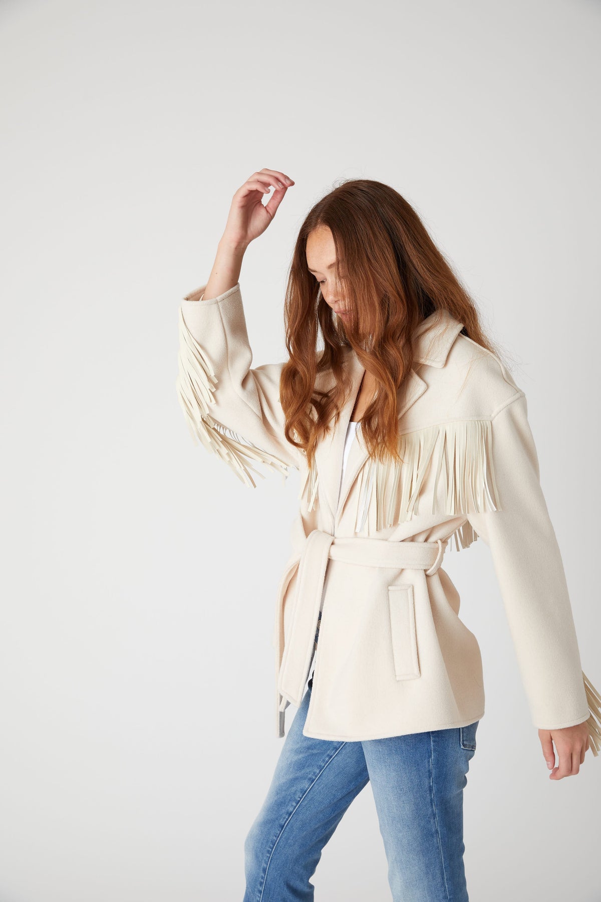 Model wearing the BLANK NYC Rodeo Star Blazer in Off White with the waist belt tied and one arm raised.