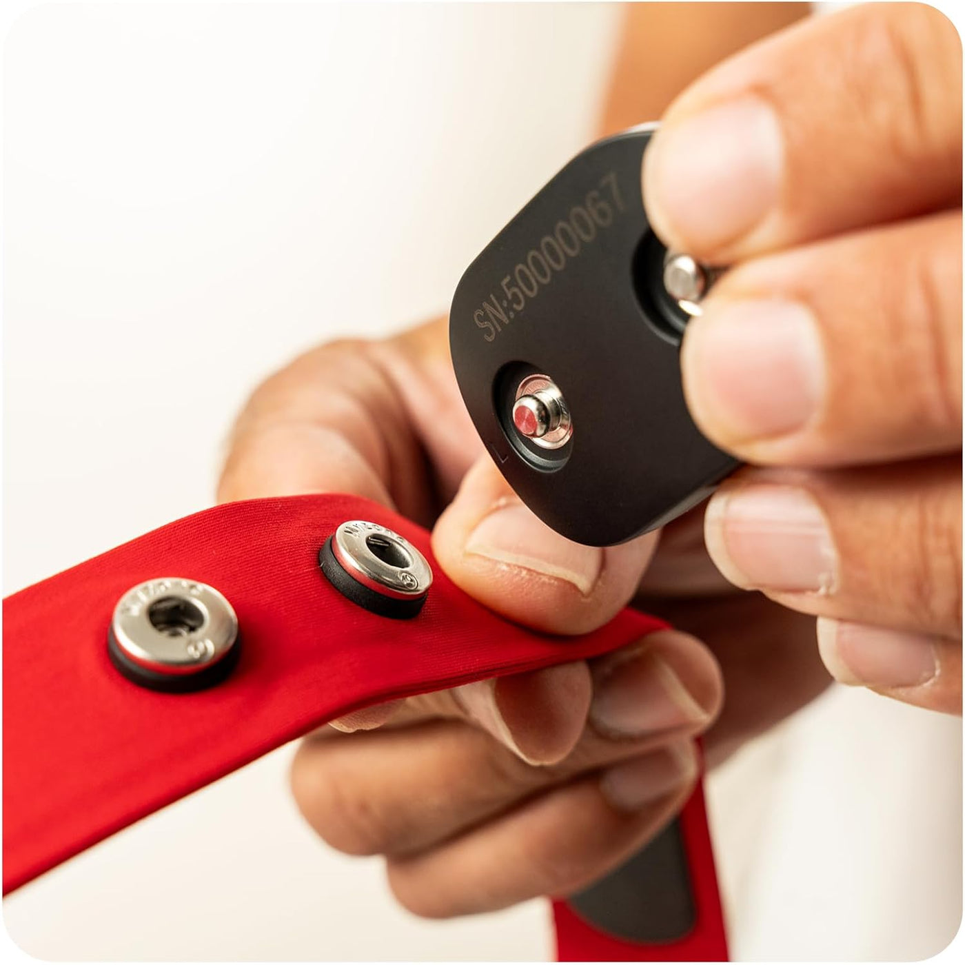 Close-up of the MYZONE Max compact heart rate monitor sensor module and snap attachments to red chest strap.