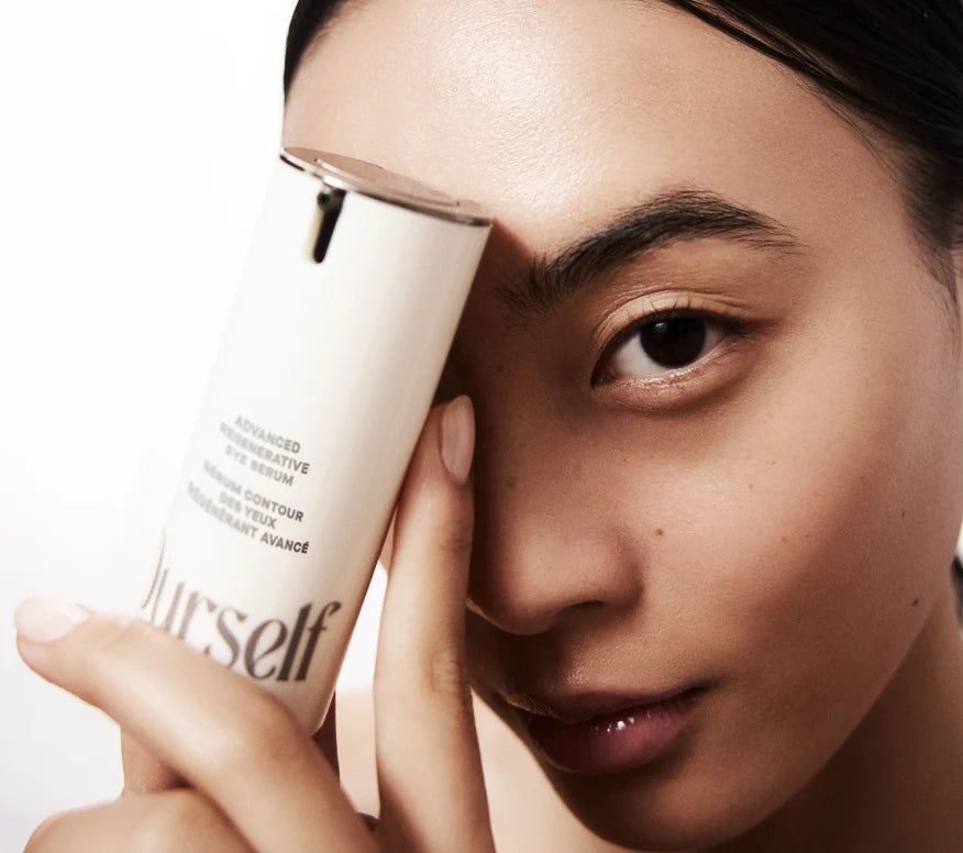 Close up of model holding bottle of Ourself Advanced Regenerative Eye Serum up to her face. 