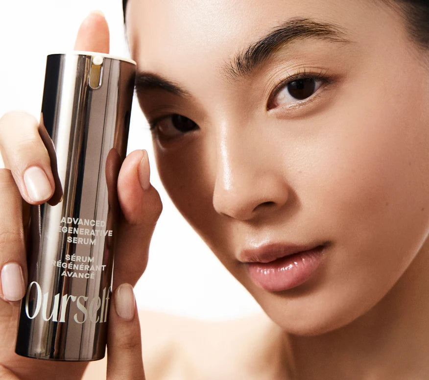 Close up of woman holding and pumping a bottle of Ourself Advanced Regenerative Serum near her face with healthy-looking skin.