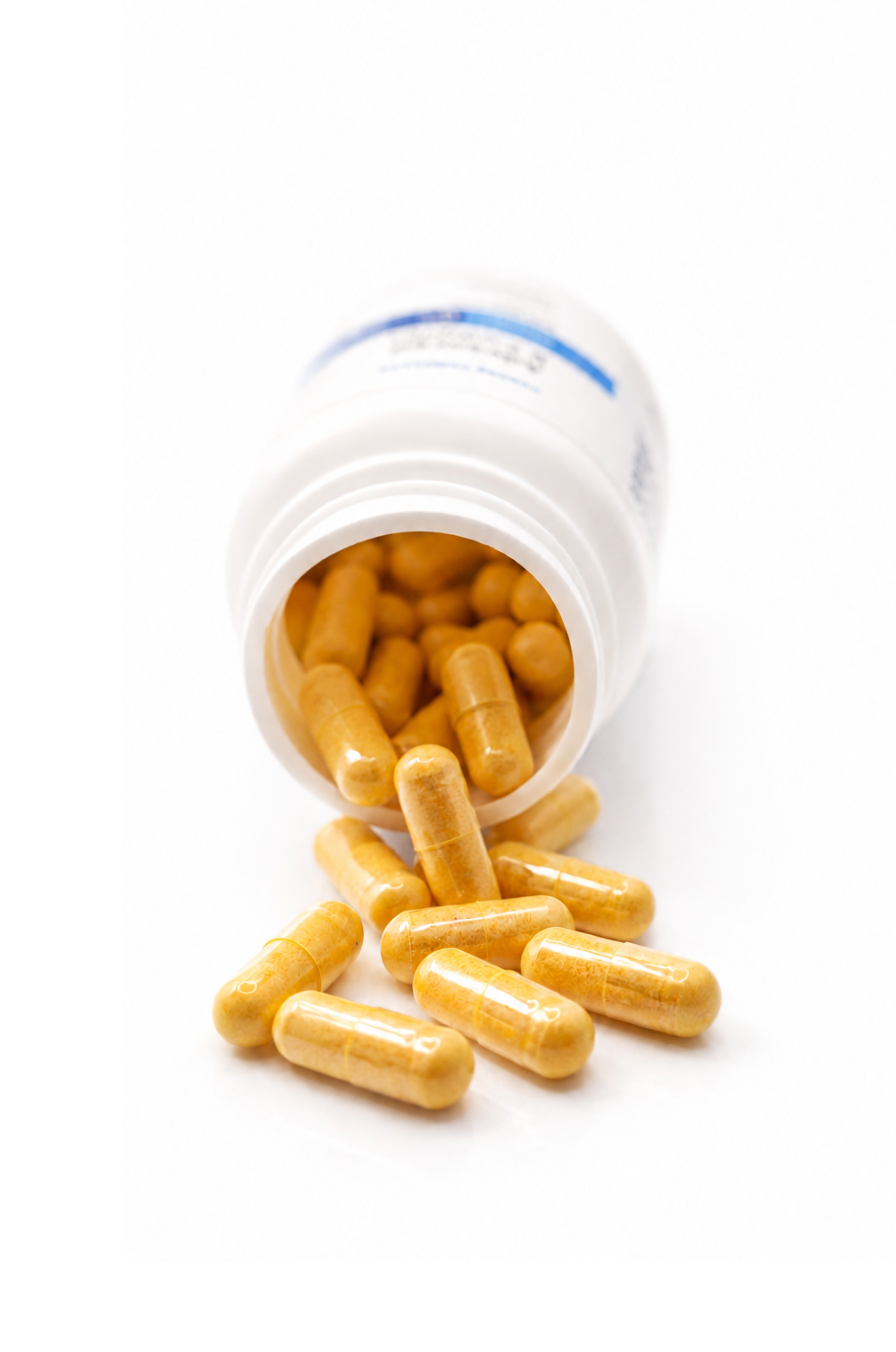 Cooper Complete Advanced B Complex yellow capsules spilling out of a white supplement bottle onto a white background