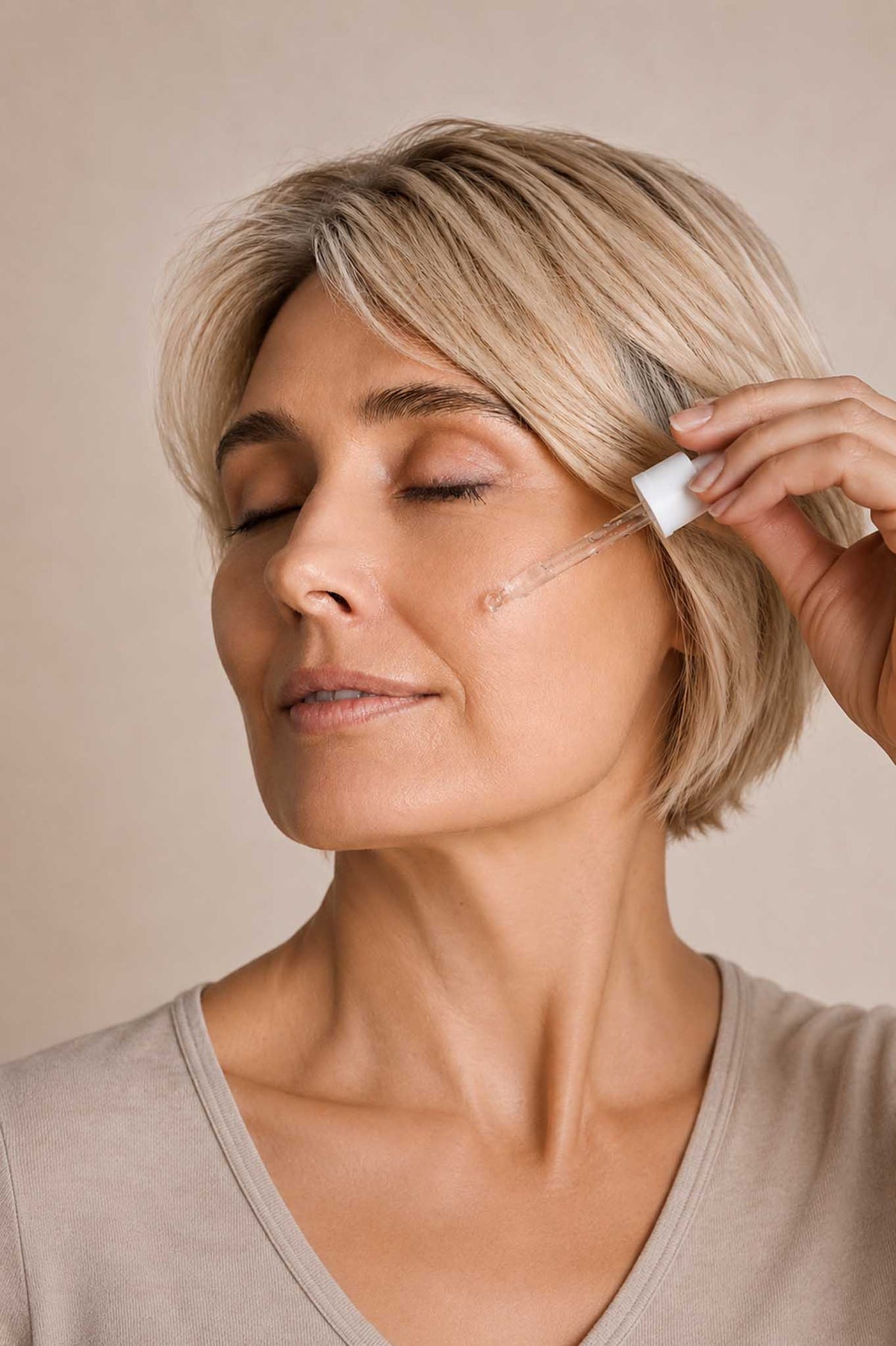 Close-up of a woman applying facial serum with a dropper to her cheek during a daily skincare routine.