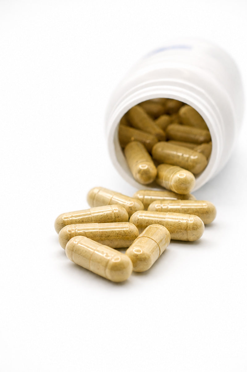 Cooper Complete Ashwagandha capsules spilling out of a white container on a white background