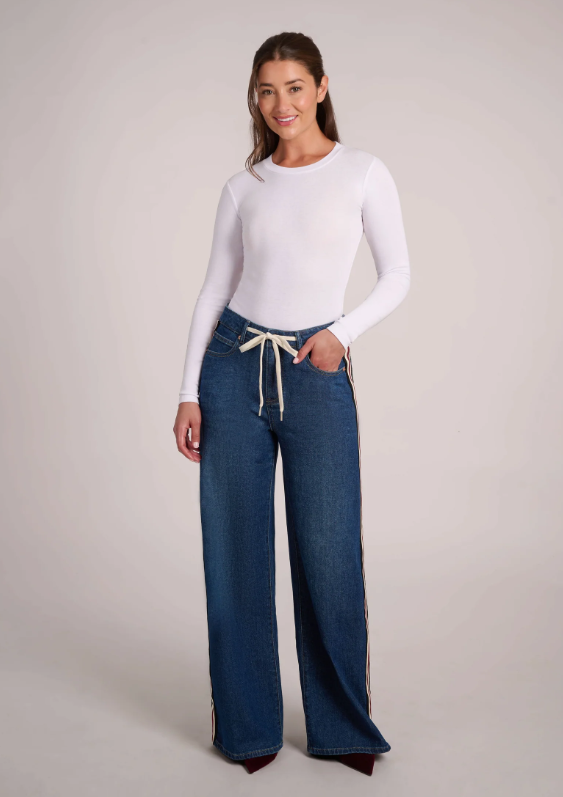 Model wearing Yoga Jeans Carina High Rise jeans with a white long-sleeve top, showing the relaxed wide-leg fit.
