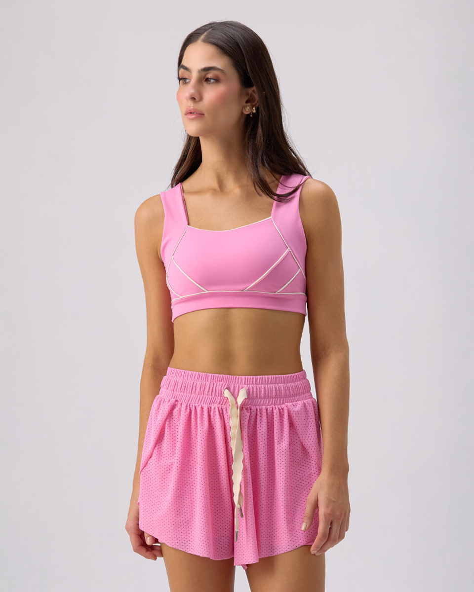Model wearing Glee x Be Fit bubble gum pink athletic sports bra and matching mesh shorts, front view.