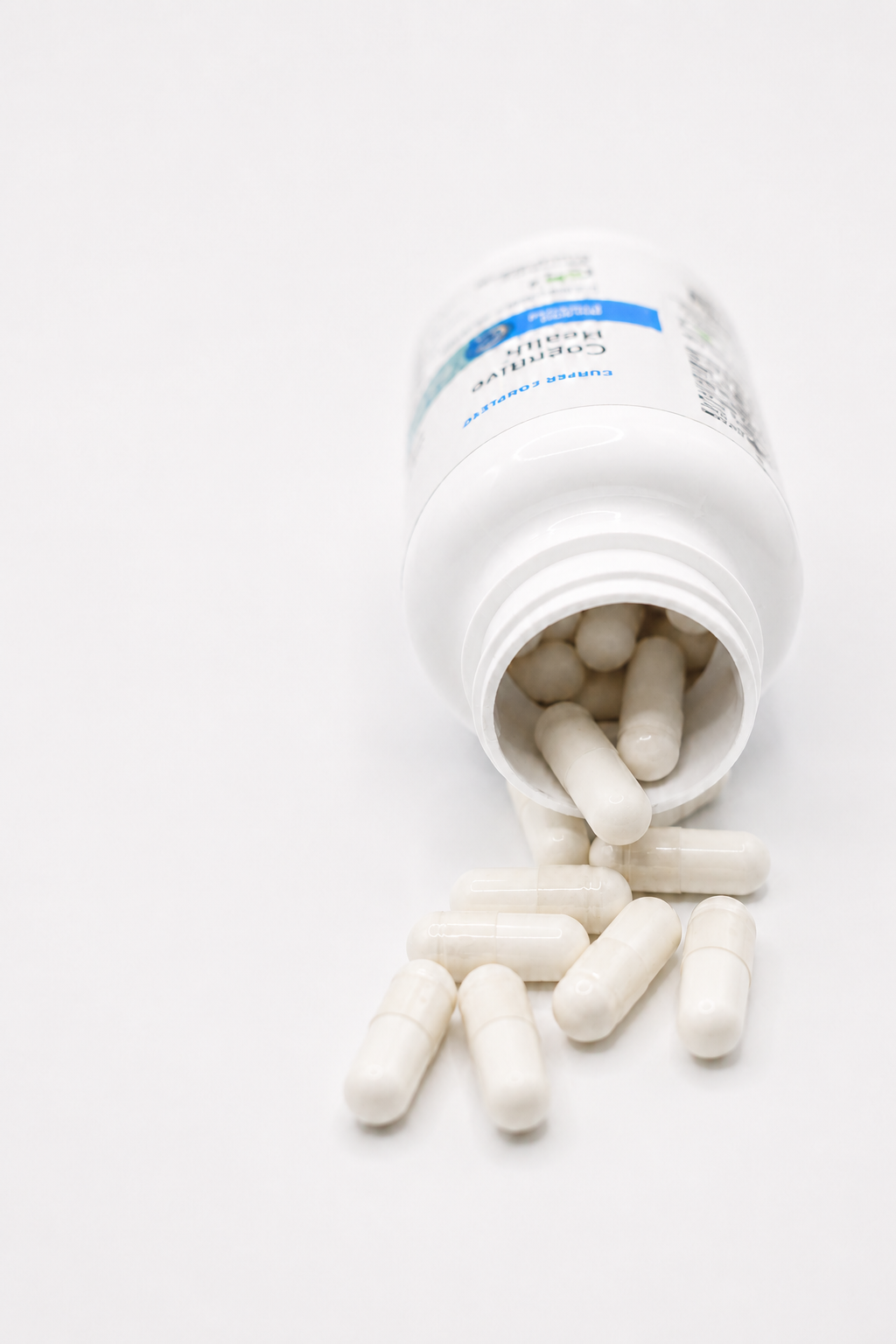 Cooper Complete Cognitive Health white plastic supplement bottle lying on its side with several off-white capsules spilling out onto a clean white surface.