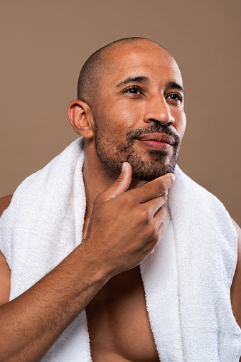 Man with a towel around his shoulders touching his beard, representing men's grooming and personal care.