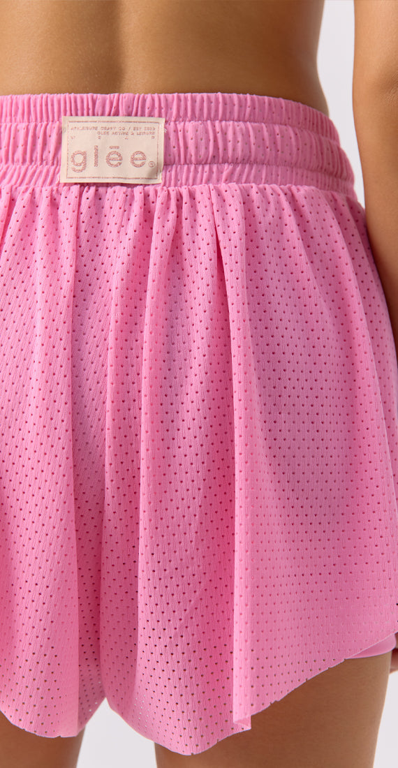Close-up of model wearing Glee x Be Fit pink mesh athletic shorts with mesh design, back view.