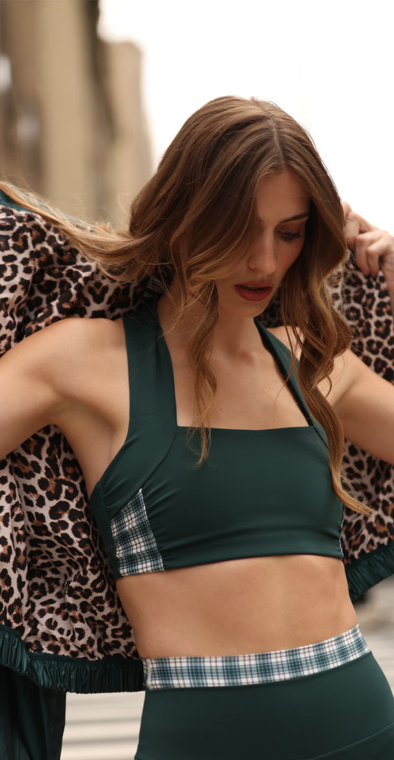 Front view of model wearing the Be Fit x Glee botanic green Elysian Garden Sports Bra with plaid side panels and matching Verdant high-rise leggings outdoors.