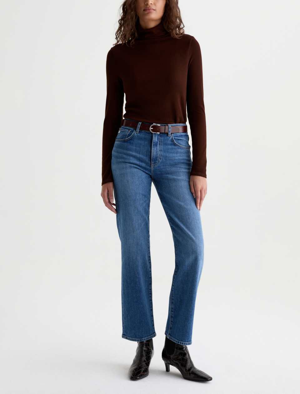 Model wearing the AG Jeans Brinley Mid-Rise Jean in Chord with a dark brown top, belt and black ankle boots.
