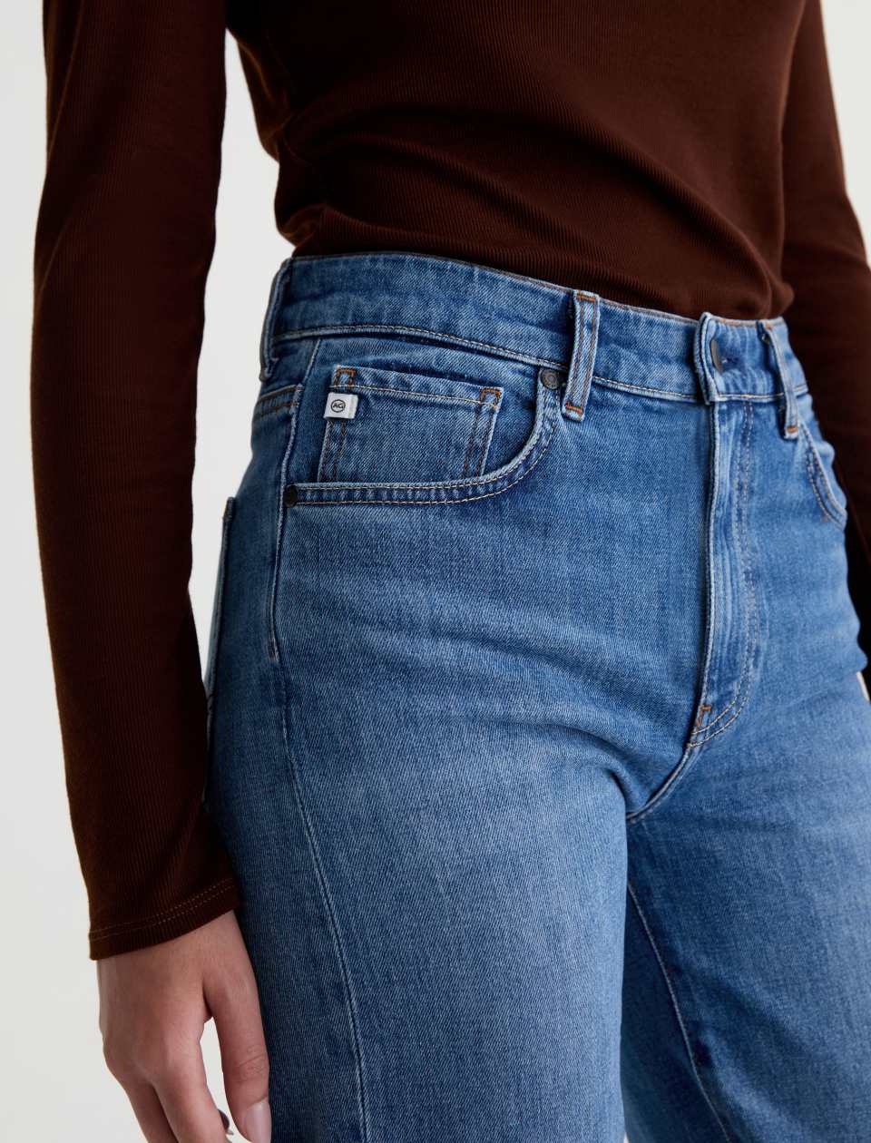 Close-up of the AG Jeans Brinley Mid-Rise Jean in Chord on a model, showing the waistband, coin pocket, stitching and whiskered denim.